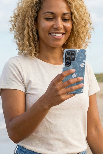 Woman on a beach holding a phone, wearing a white t-shirt and blue shorts.